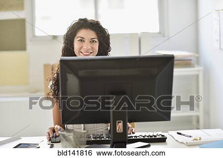 Stock Photograph - Mixed race businesswoman working on computer at desk in office. Fotosearch