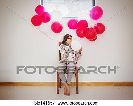 Stock Photo - Mixed race girl blowing up balloons for party. Fotosearch