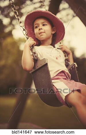 Stock Photo - Mixed race girl playing on swing on playground. Fotosearch