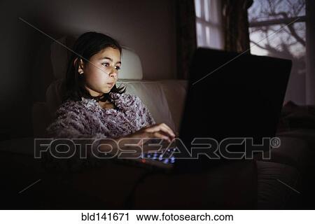 Stock Image - Mixed race girl using laptop at night. Fotosearch