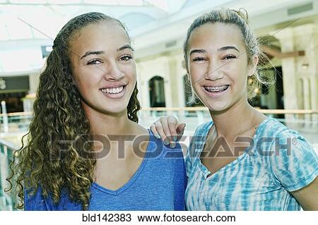 Stock Image - Mixed race teenage girls smiling at shopping mall. Fotosearch