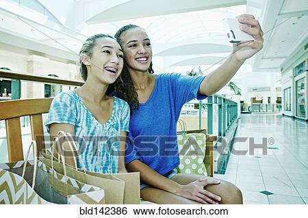 Stock Photograph - Mixed race teenage girls taking cell phone photograph at shopping mall. Fotosearch
