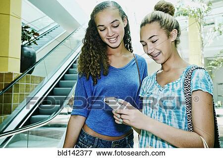 Mixed race teenage girls using cell phone near escalator at shopping mall View Large Photo Image Stock Photo - Mixed race teenage girls using cell phone near escalator at shopping mall. Fotosearch