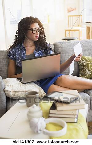 Mixed race woman paying bills on laptop on sofa View Large Photo Image Stock Image - Mixed race woman paying bills on laptop on sofa. Fotosearch