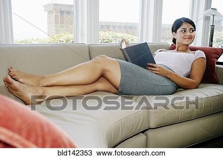 Stock Image - Mixed race woman reading book on sofa. Fotosearch