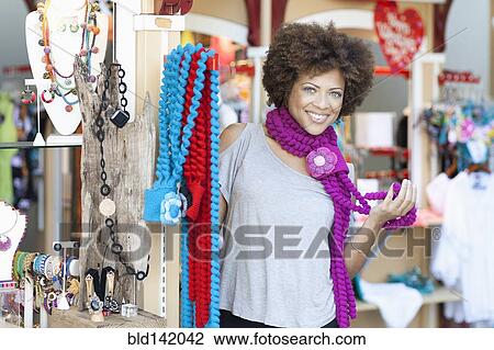 Stock Image - Mixed race woman trying on necklaces in store. Fotosearch