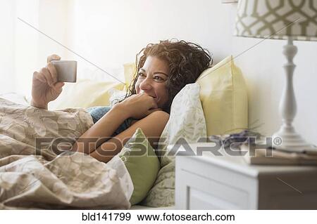 Stock Photo - Mixed race woman using cell phone in bed. Fotosearch