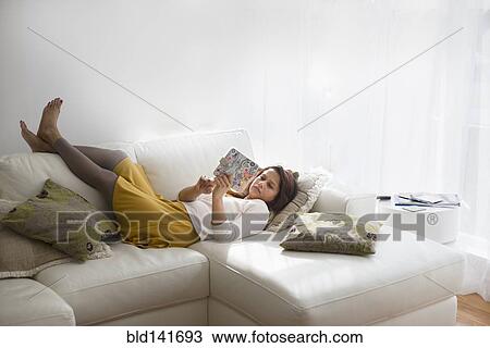 Stock Image - Mixed race woman using digital tablet on living room sofa. Fotosearch