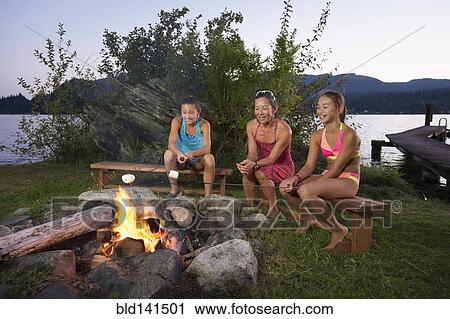 Stock Image - Mother and children roasting marshmallows over campfire. Fotosearch