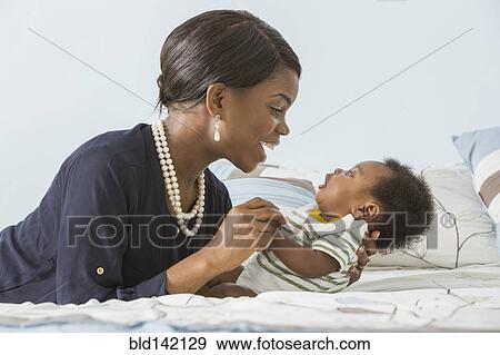 Stock Photo - Mother cradling baby son on bed. Fotosearch