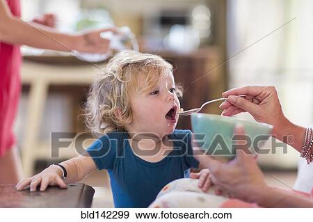 Stock Photo - Mother feeding baby son from bowl. Fotosearch