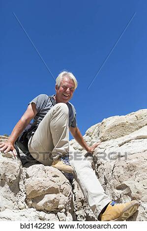Stock Image - Older Caucasian man climbing rock formations. Fotosearch