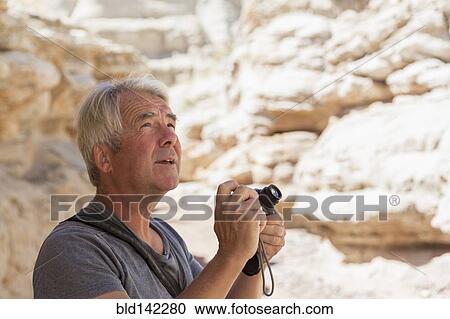 Stock Image - Older Caucasian man photographing rock formations. Fotosearch