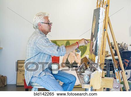 Stock Photography - Older Hispanic artist painting in studio. Fotosearch