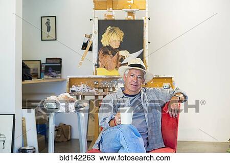 Stock Image - Older Hispanic artist relaxing in studio. Fotosearch
