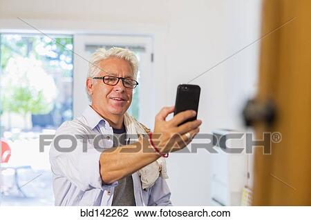 Stock Image - Older Hispanic artist taking cell phone photograph of art in studio. Fotosearch