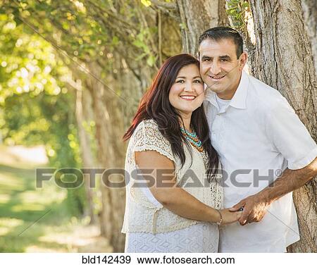 Stock Photo - Older Hispanic couple hugging near tree. Fotosearch