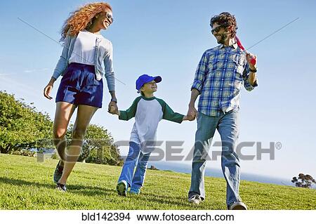 Picture - Parents and daughter walking in grassy field. Fotosearch
