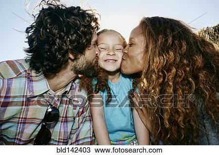 Stock Image - Parents kissing cheeks of daughter outdoors. Fotosearch