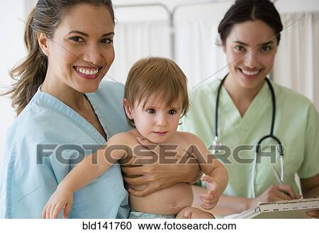 Stock Image - Pediatrician doctor and nurse holding baby girl in hospital. Fotosearch