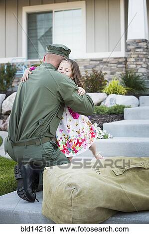Stock Image - Returning Caucasian soldier hugging daughter on front stoop. Fotosearch