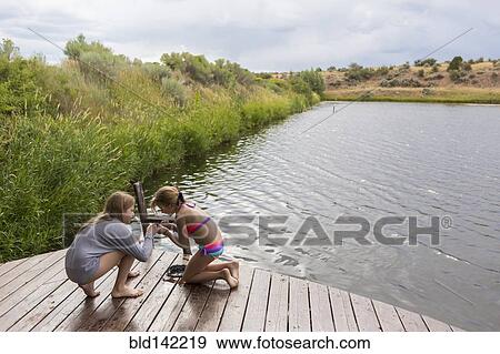 Stock Photo - Sisters playing together on wooden dock near lake. Fotosearch