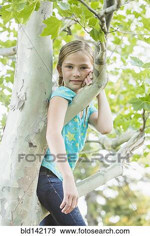 Stock Photo - Smiling Caucasian girl climbing tree outdoors. Fotosearch