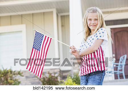 Stock Photography - Smiling Caucasian girl waving American flag near house. Fotosearch