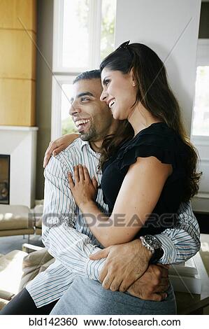 Stock Image - Smiling couple hugging in living room. Fotosearch