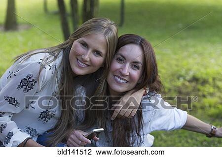 Stock Image - Smiling Hispanic women hugging outdoors. Fotosearch