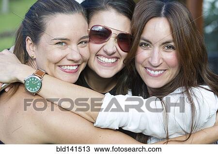 Stock Image - Smiling Hispanic women hugging outdoors. Fotosearch