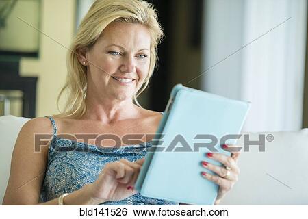 Stock Photograph - Smiling woman using digital tablet on sofa. Fotosearch