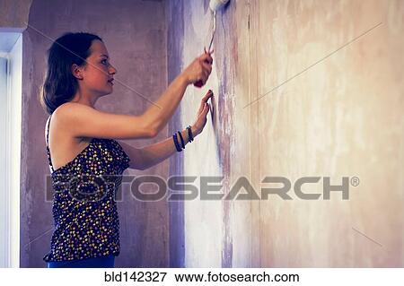 Stock Photo - Woman painting wall with paint roller. Fotosearch
