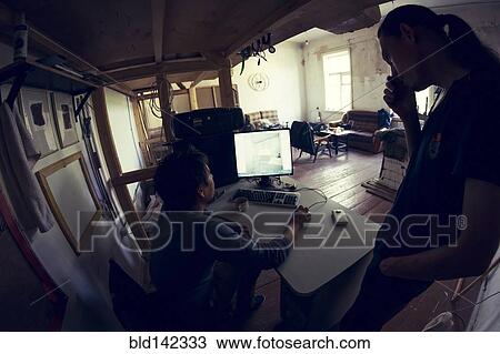 Stock Image - Young men using laptop together under loft bed. Fotosearch