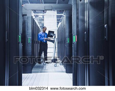 Picture - Black businessman using computer in server room. Fotosearch