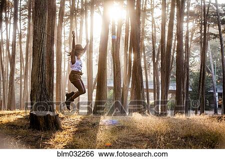 Stock Photograph - Black woman jumping from stump in sunny forest. Fotosearch