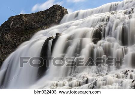 Stock Image - Blurred view of waterfall flowing over rock formations. Fotosearch