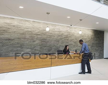 Stock Photograph - Businessman talking to receptionist at office front desk. Fotosearch