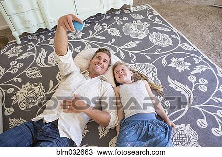 Stock Image - Caucasian father and daughter taking cell phone selfie on floor. Fotosearch