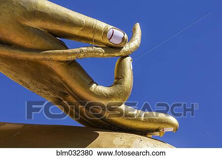 Stock Image - Close up of golden hand statue against blue sky. Fotosearch