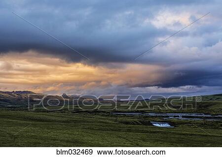 Stock Photo - Clouds over green fields in rural landscape. Fotosearch