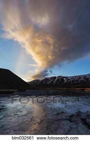 Stock Image - Clouds over riverbed and mountains in remote landscape. Fotosearch