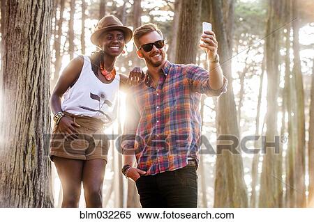 Stock Photography - Couple taking cell phone picture in sunny forest. Fotosearch