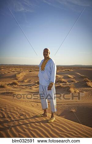 Stock Image - Guide smiling on sand dunes in desert landscape. Fotosearch