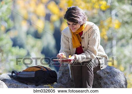 Stock Photography - Mixed race woman reading journal on rock. Fotosearch