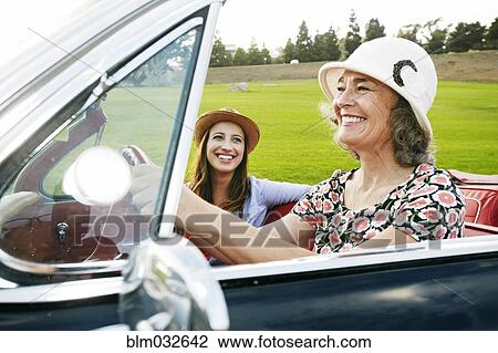 Stock Image - Mother and daughter driving in classic convertible. Fotosearch
