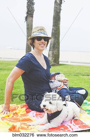 Stock Photograph - Mother and newborn baby sitting with dog in park. Fotosearch