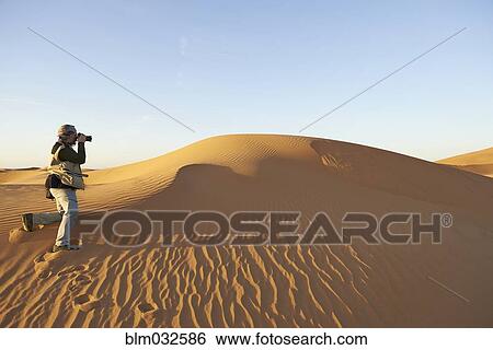 Tourist photographing sand dunes in desert landscape View Large Photo Image Stock Photograph - Tourist photographing sand dunes in desert landscape. Fotosearch