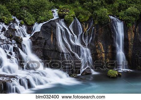 Stock Image - Waterfall flowing over rock formations to lake. Fotosearch