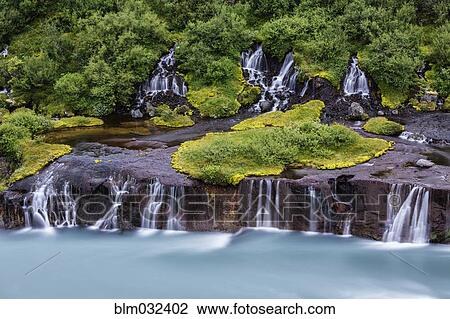 Stock Image - Waterfall flowing over rock formations to lake. Fotosearch